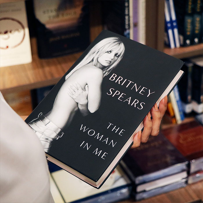 Person holding the book titled Britney Spears The Woman In Me, related to Britney Spears net worth and wealth after conservatorship.