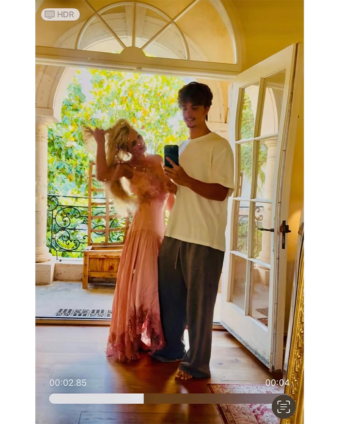 Britney Spears posing in pink dress with a man taking a mirror selfie, reflecting on her net worth after conservatorship.