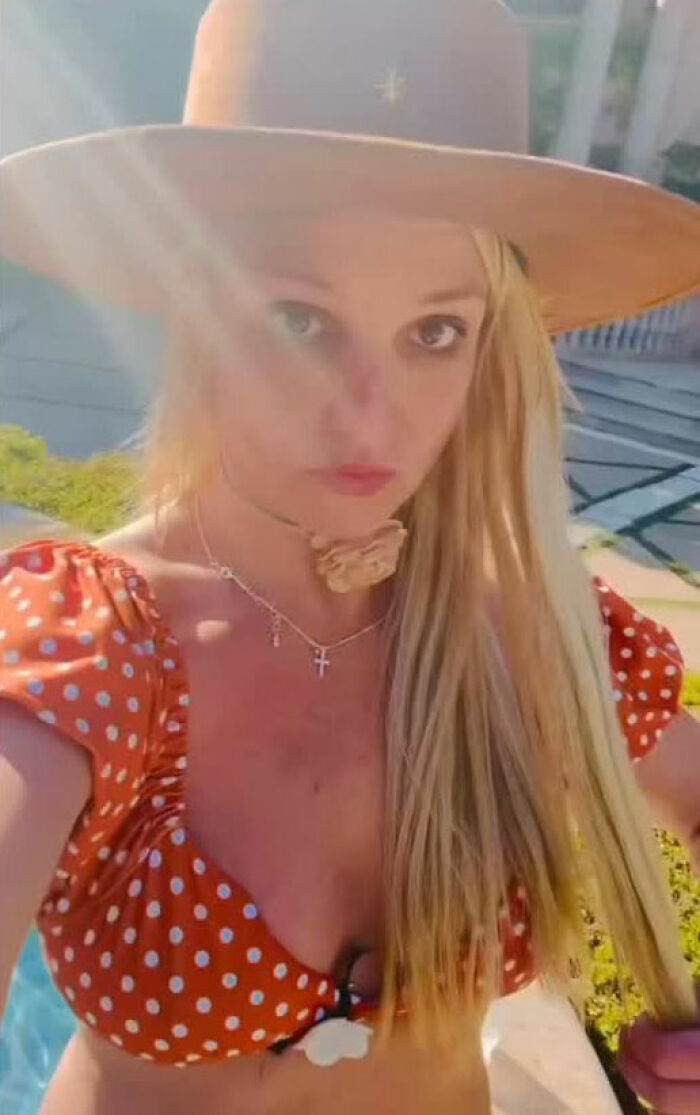 Britney Spears outdoors wearing a hat and polka dot top with sunlight glare, highlighting a nip slip during her dance.