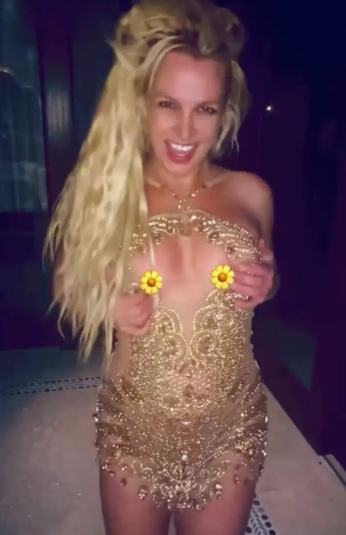 Britney Spears in a gold minidress during a dance with a nip slip moment, smiling with long blonde hair.