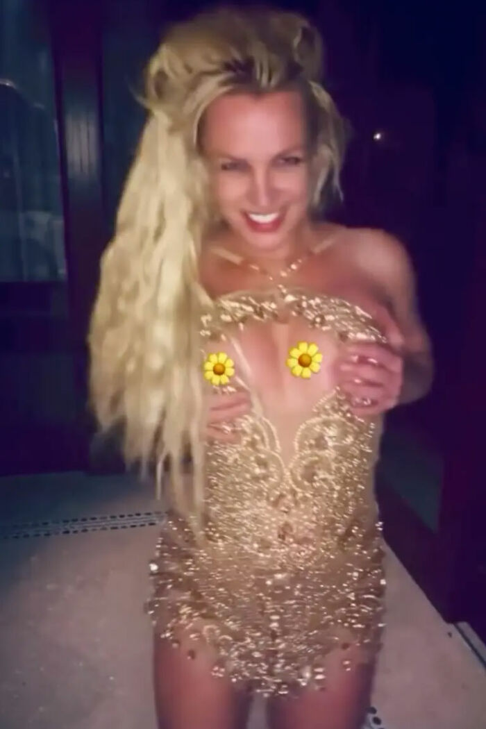 Britney Spears in a gold minidress experiencing a wardrobe malfunction during a dance performance at night.