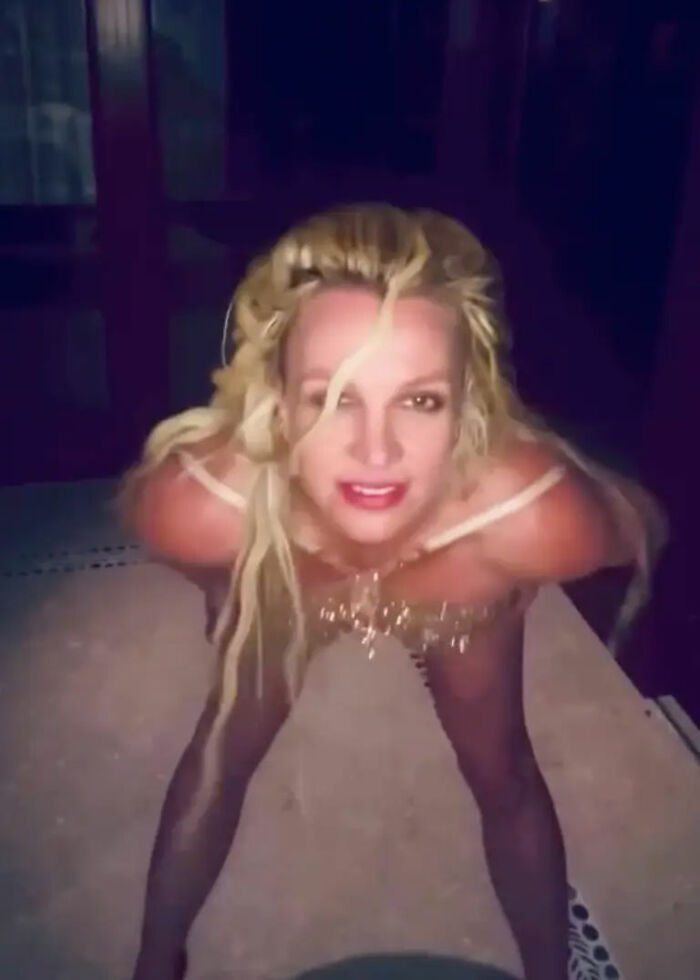 Britney Spears wearing a gold minidress performing a dance, captured during a nip slip moment.