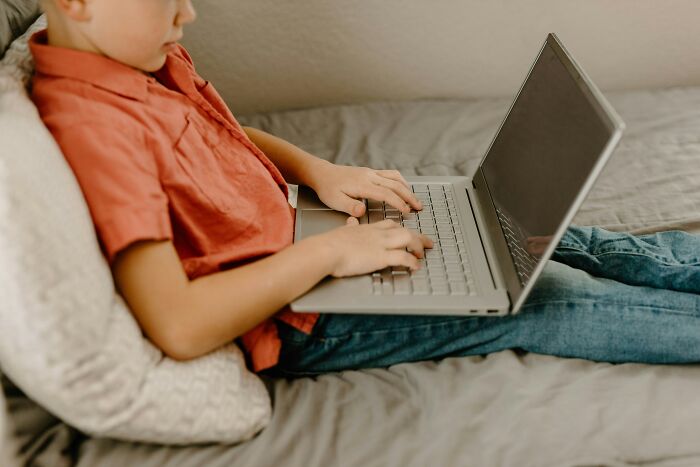 Child in red shirt using a laptop on bed, illustrating how Reddit is not for the faint of heart in online discussions.