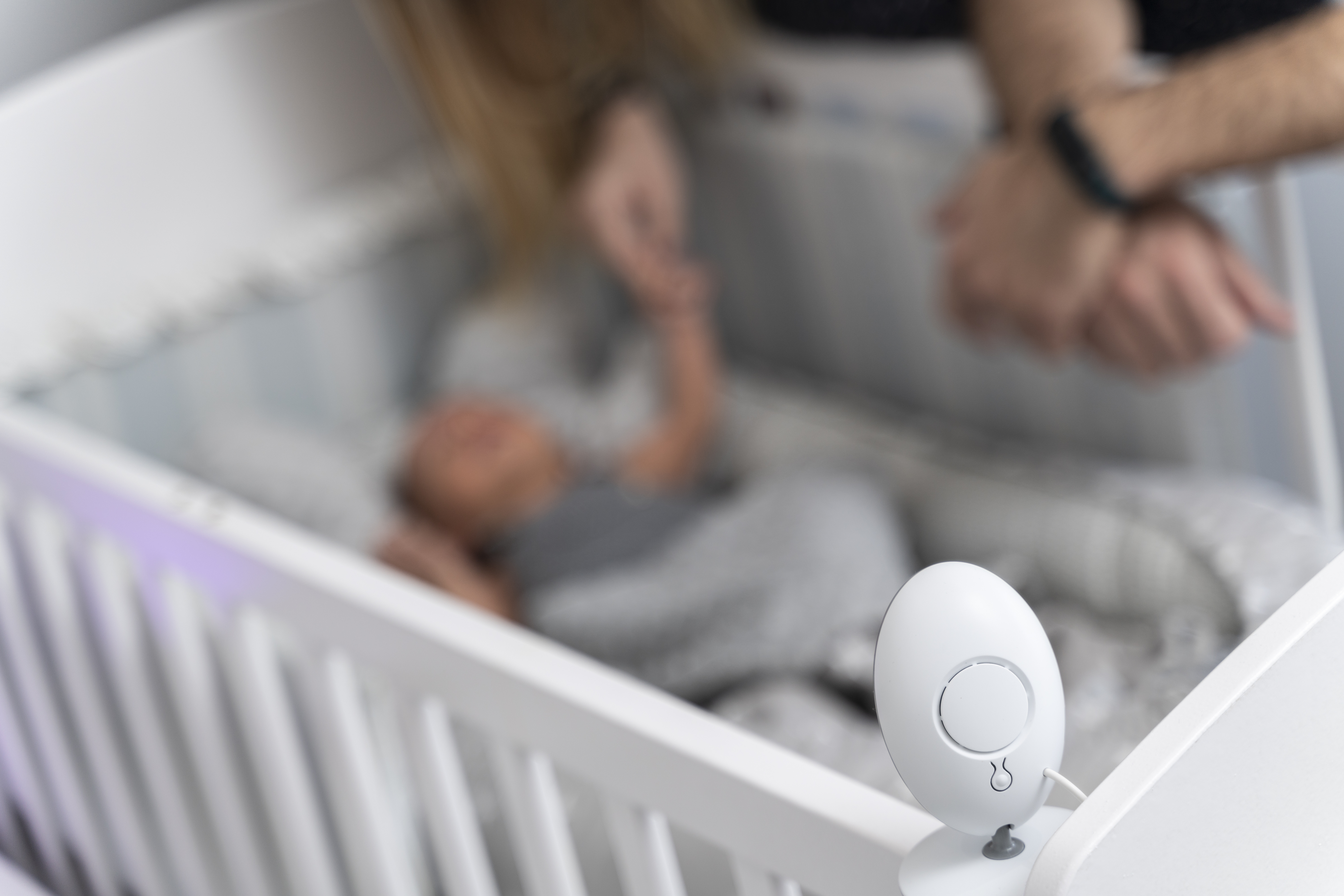 Baby monitor camera in focus on crib edge as mom watches over sleeping infant showing baby cam access concerns.