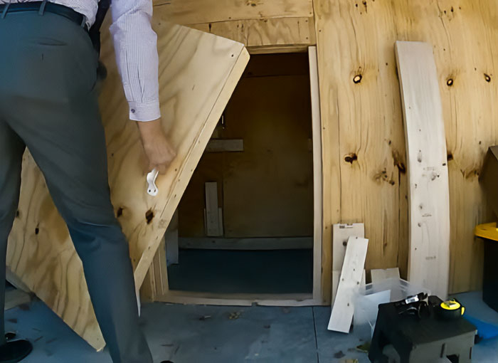 Man opening wooden door leading to a soundproof bunker resembling a captive space linked to a stalker incident.