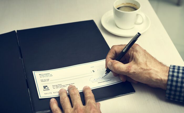Person signing a check at a desk with coffee, illustrating concepts related to wealth gap and financial disparity.