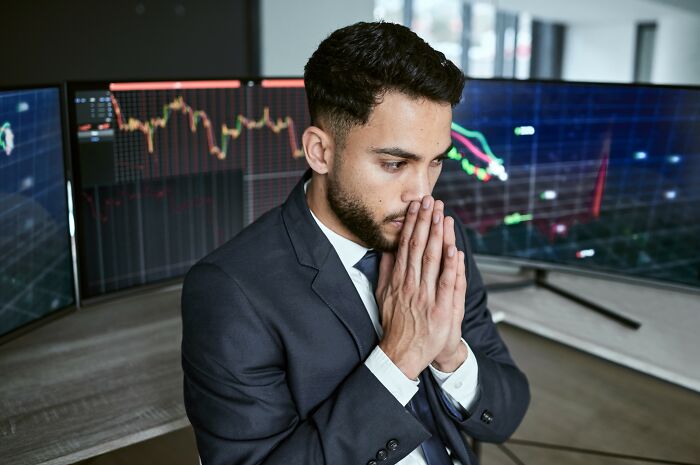 A thoughtful man in a suit contemplates financial charts on multiple screens, reflecting on smartest kids in class.