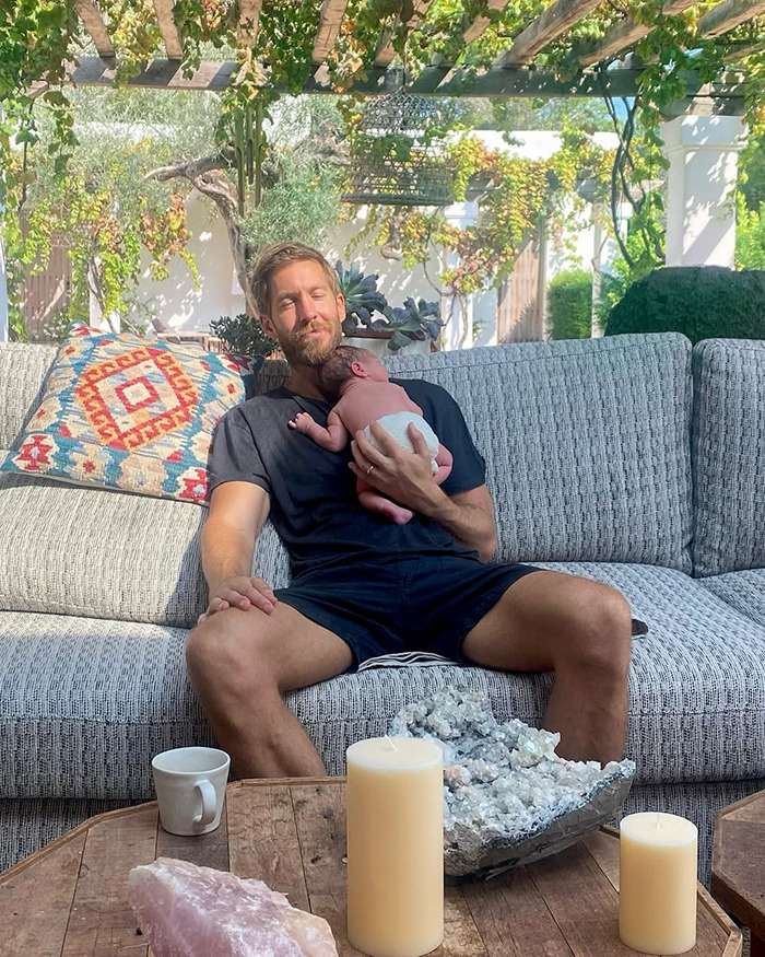 Calvin Harris holding newborn baby on couch with candles and decorative stones in outdoor setting. - 1