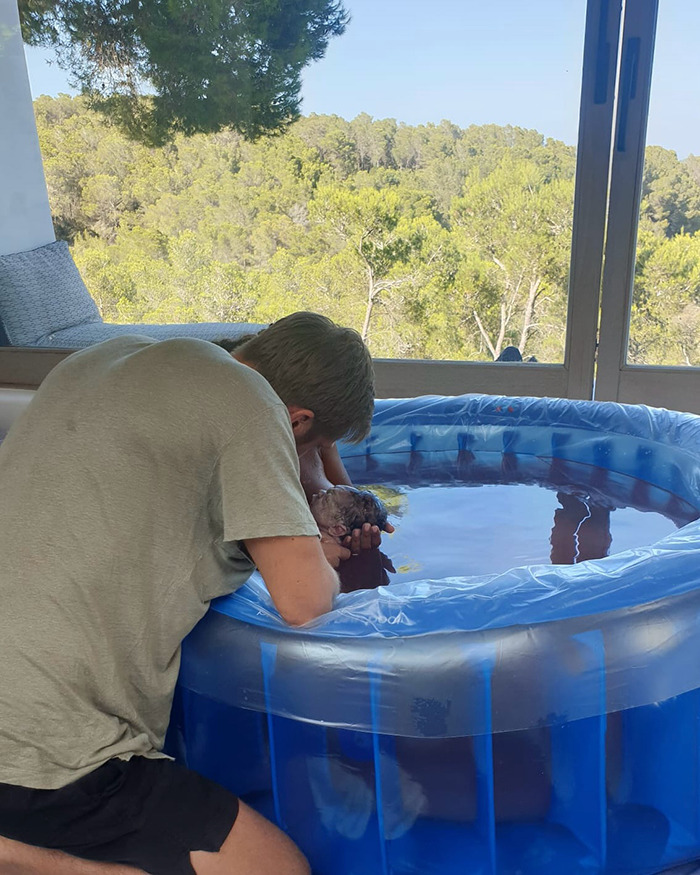 Man leaning over a birthing pool holding a newborn baby, related to Calvin Harris placenta encapsulation process. - 3