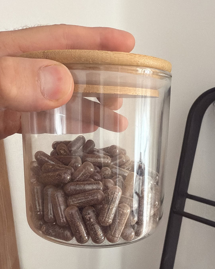 Hand holding a glass jar filled with placenta capsules during the encapsulation process after birth announcement. - 6