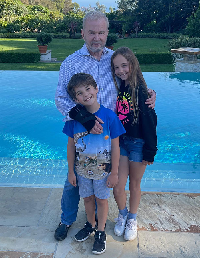 Man with two children standing near a pool in a backyard, unrelated to Katy Perry bikini breakup rumored fling legal drama.