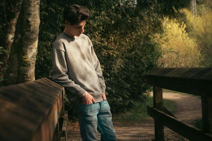 Teenage boy leaning on a wooden bridge in a park, reflecting on creative ways to avoid babysitting duties.