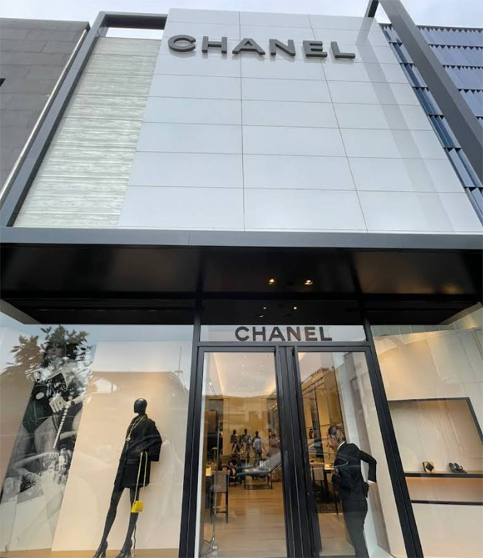 Chanel store exterior with mannequins in window displays and a person entering the luxury fashion boutique.