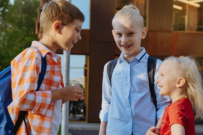 Three smiling children with backpacks talking outside, illustrating stories of people getting savagely rejected.