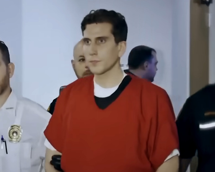 Bryan Kohberger in jail wearing a red outfit with red hands while surrounded by law enforcement officers. Bryan Kohberger in jail wearing a red outfit with red hands while surrounded by law enforcement officers.