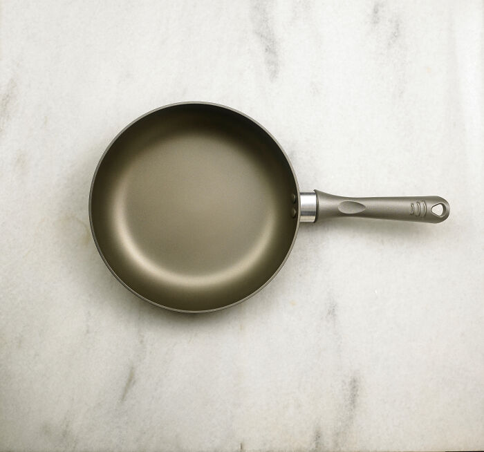 Empty non-stick frying pan with handle placed on a light marble surface, illustrating terrifying things people swear they've seen.