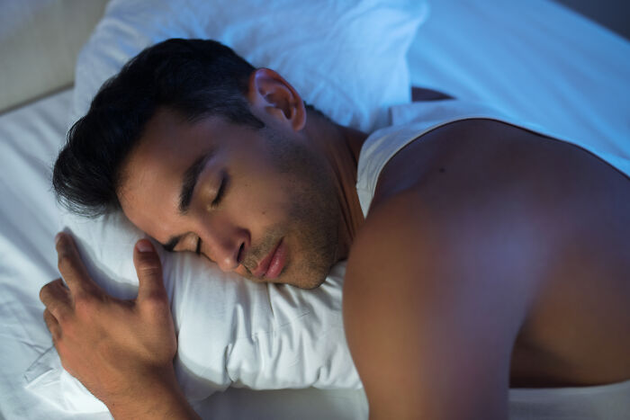 Young man sleeping peacefully on white pillow in dim light, evoking feelings of terrifying things people swear they've seen