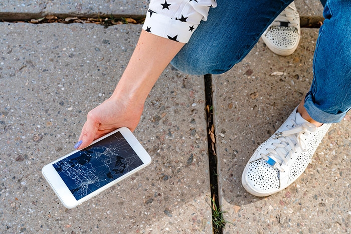 Person holding a c*****d smartphone on pavement, illustrating frustration with clumsy girlfriend destroying his stuff.