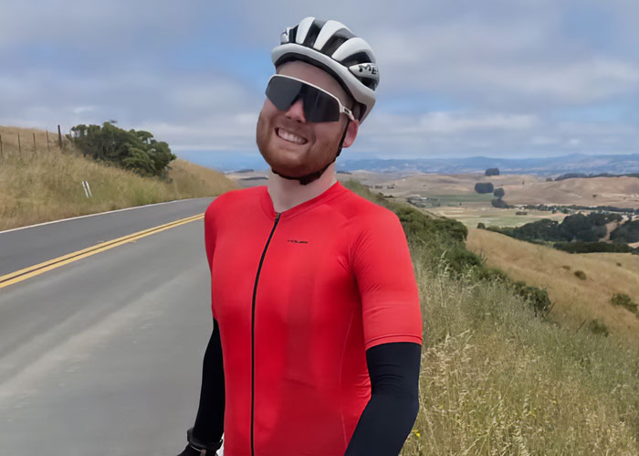 Cyclist in red gear standing on rural road, representing a good Samaritan trying to protect helpless mom and children.