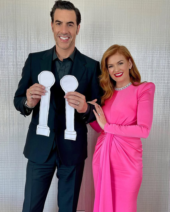 Two people posing together, with one holding paper cutouts, related to columnist criticism of Sacha Baron Cohen’s Marvel body. - 12