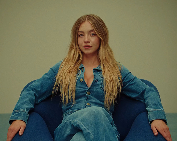 Sydney Sweeney seated in a blue outfit, featured in Birds Of A Feather alongside comedian Matt Rife backing her after viral backlash.
