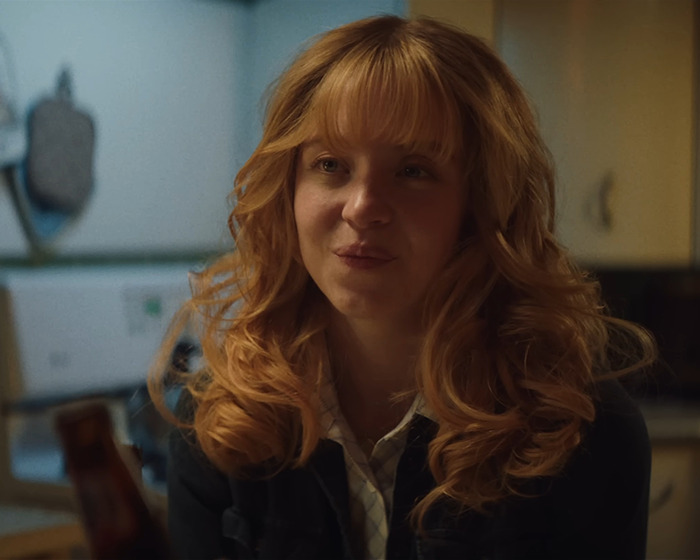 Sydney Sweeney in a dimly lit room, with curly hair, relating to the viral ad backlash and Matt Rife support.