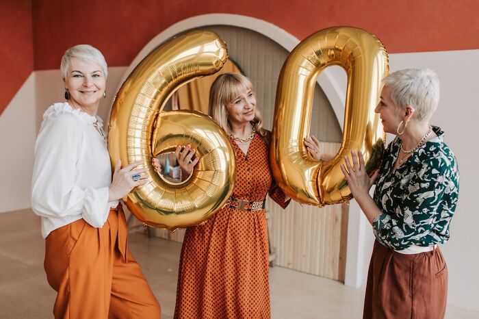 Three women celebrating with gold number 60 balloons, illustrating concept time facts about aging and milestones.