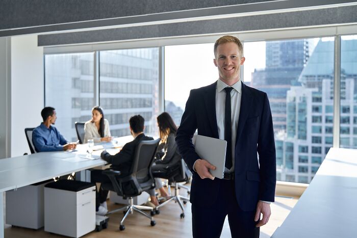 Young professional in a suit holding a laptop in a modern office, representing smartest kids in their class success.