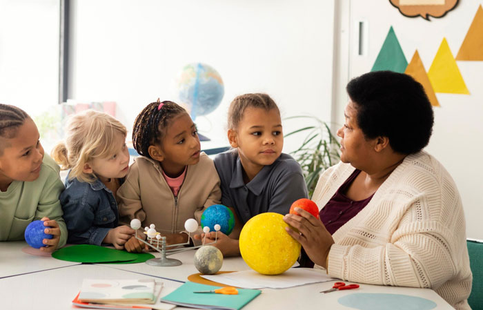Teacher conducting unconscious bias training with diverse children using a solar system model in a classroom setting.
