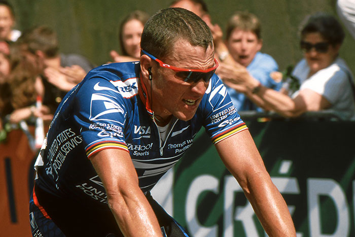 Professional cyclist wearing sunglasses and team jersey, showing determination during a competitive race moment.