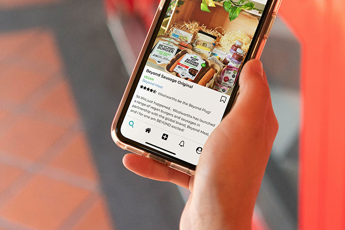 Person holding a smartphone displaying a social media post about Beyond Sausage Original vegan meat products.