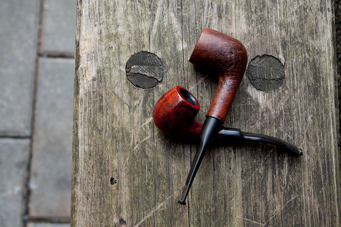 Two vintage wooden smoking pipes resting on weathered wooden surface, representing conspiracy theorists concept.