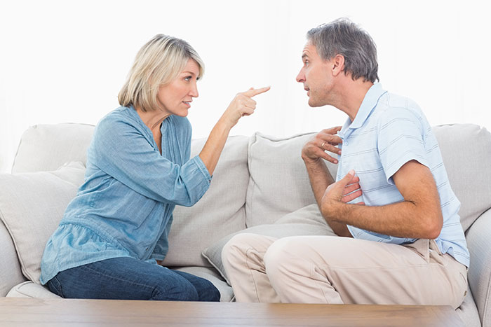 Middle-aged couple arguing passionately on a couch, illustrating conflict after man's compliment to girlfriend's mom.
