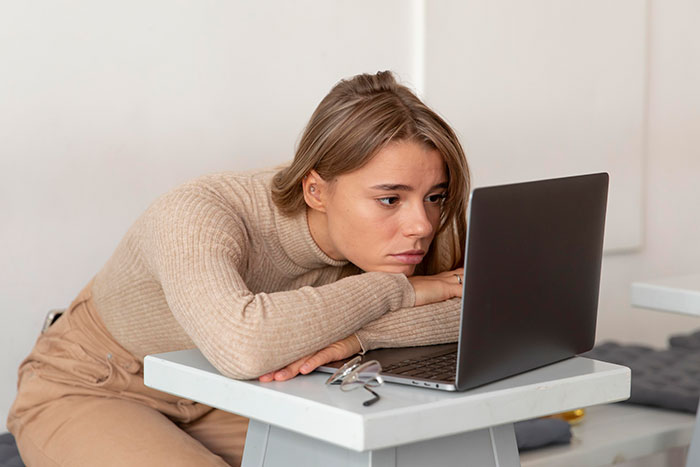 Young woman looking distressed while resting her head on crossed arms in front of a laptop, reflecting mental health struggles