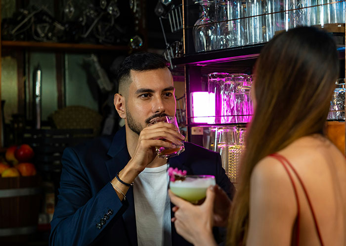 Man and woman enjoying drinks at a bar, illustrating the ups and downs of a partner who went from rags to riches.