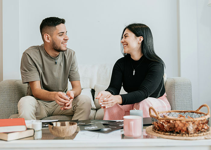 Couple smiling and talking on a couch, representing the ups and downs of having a partner who went from rags to riches.