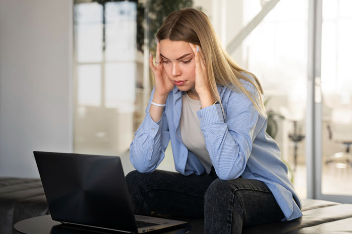 Young woman stressed while working on laptop, experiencing coworker misgenders related to Muslim religion in office setting