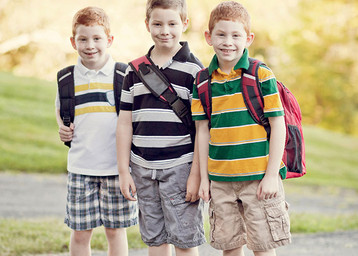 Three young boys with backpacks standing outdoors, illustrating the impact of horrible names on children.