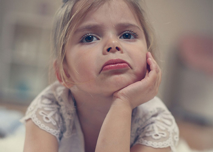Sad young girl resting her face on her hand, reflecting pain caused by horrible names like Jam Metallica.