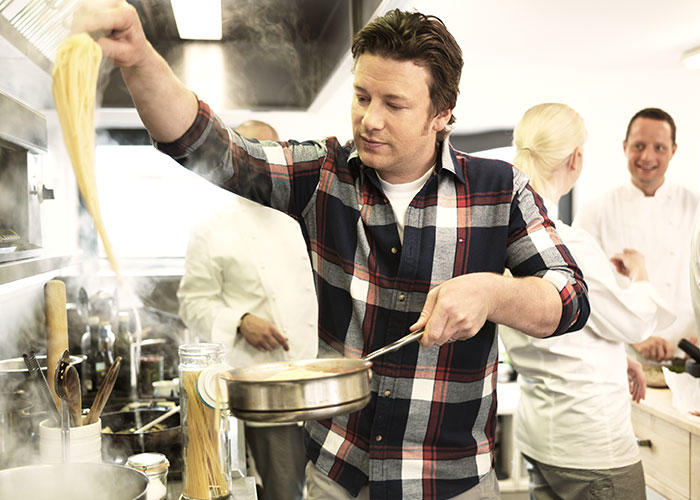 Man cooking pasta in a busy kitchen with chefs in the background, illustrating jam metallica concept humorously.