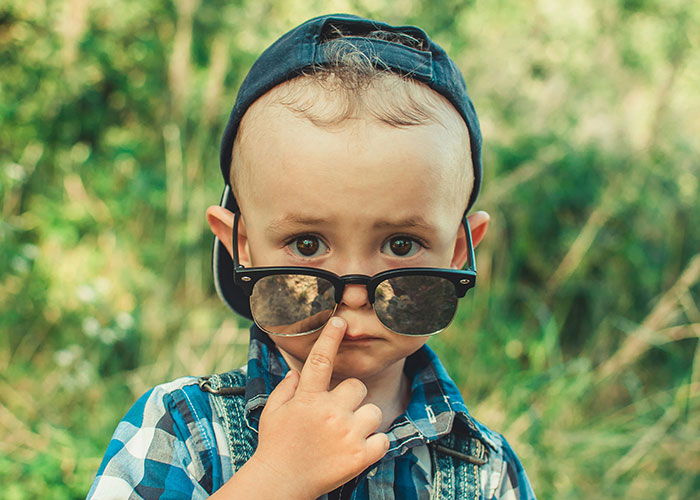 Toddler wearing sunglasses and a backwards cap outdoors, reflecting on unusual names causing lifelong pain.