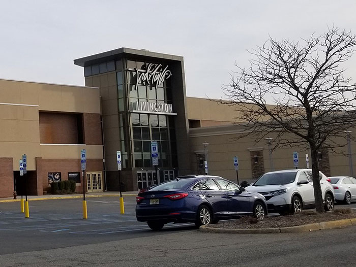 Mall exterior with empty parking lot and bare tree, evoking creepy vibes at an abandoned shopping center.