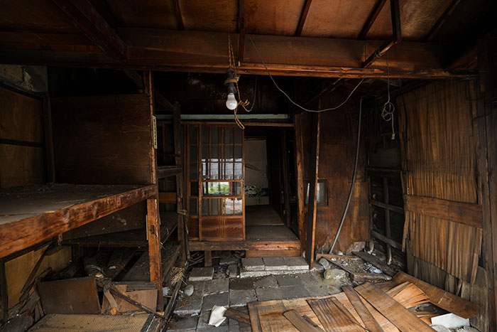 Interior of an abandoned wooden structure with debris, dim lighting, and a creepy vibe evoking eerie abandoned places.