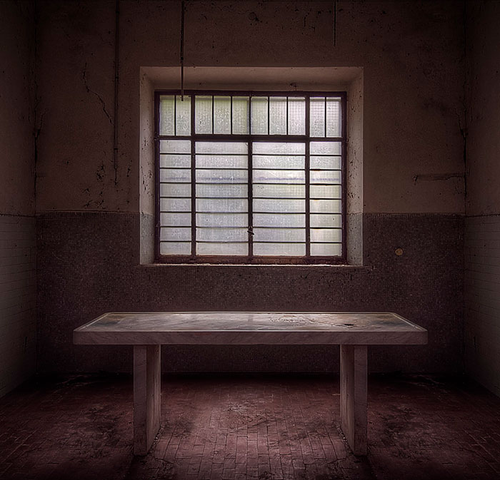 Empty room with a single table under a barred window, evoking creepy vibes from abandoned places people visited.