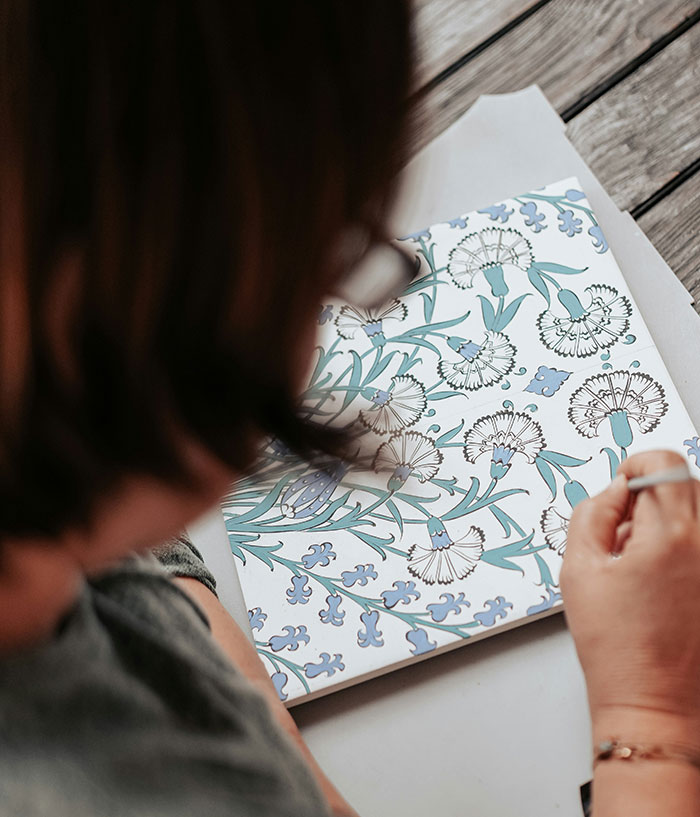 Person painting floral patterns on a tile, creating art inspired by places giving off creepy vibes.