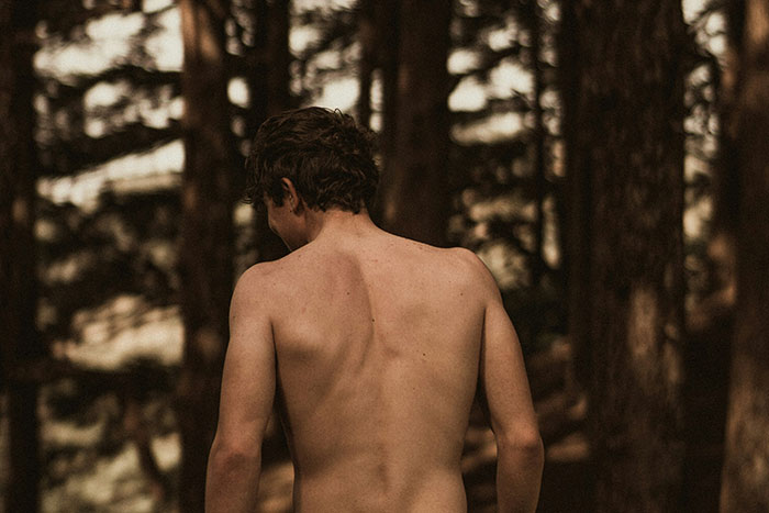 Shirtless person walking through a dense forest, evoking the creepiest things seen outdoors in a terrifying outdoor setting.