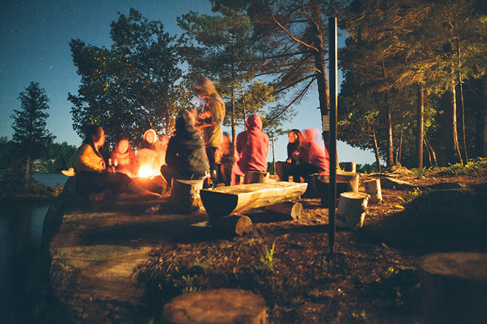 Group of people gathered around a campfire outdoors at night, sharing creepy and terrifying outdoor stories.