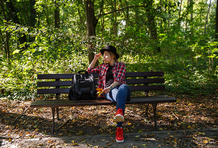 Young woman sitting on a bench in the woods, surrounded by nature, evoking the creepiest things seen outdoors vibe.