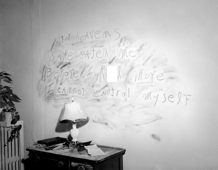 Creepy and unsettling message smeared on a wall above a cluttered desk in a dimly lit room, creating eerie vibes.