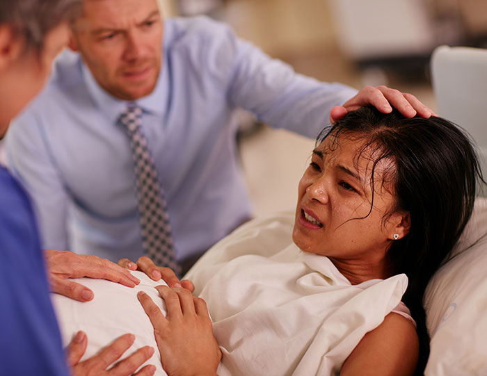 Woman in labor lying on a hospital bed with concerned medical staff assisting during a difficult delivery scene.